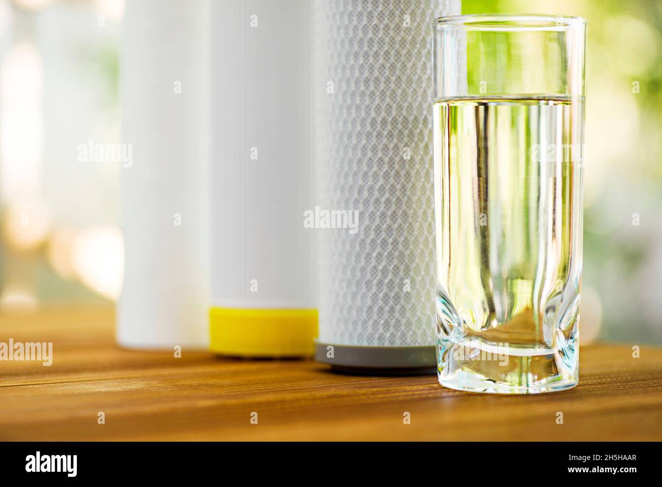 A glass of purified water and filter cartridges on wooden table on green natural background Stock Photo