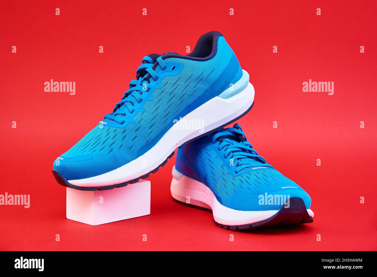 Blue running sneakers on red background. Pair of sport male shoes for  fitness on geometic cube podium Stock Photo - Alamy