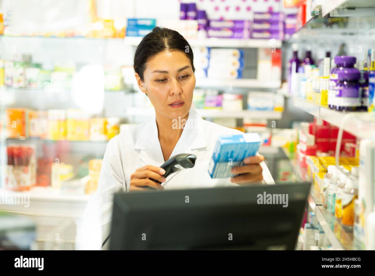 Portrait of female pharmacist working at the cash register in pharmacy scans barcode on