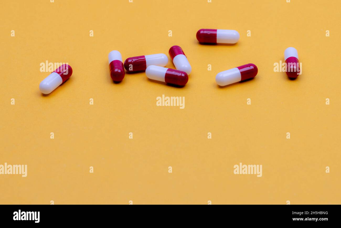 Antibiotic capsule pills on yellow background. Pharmaceutical industry. Prescription drug. Red-white capsule pills. Pharmaceutical product. Pharmacy Stock Photo
