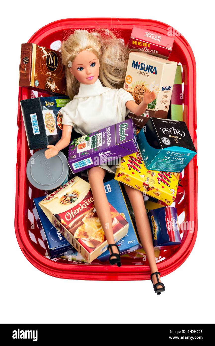 Directly above shot of woman doll in a miniature shopping basket full of various merchandise on white background Stock Photo