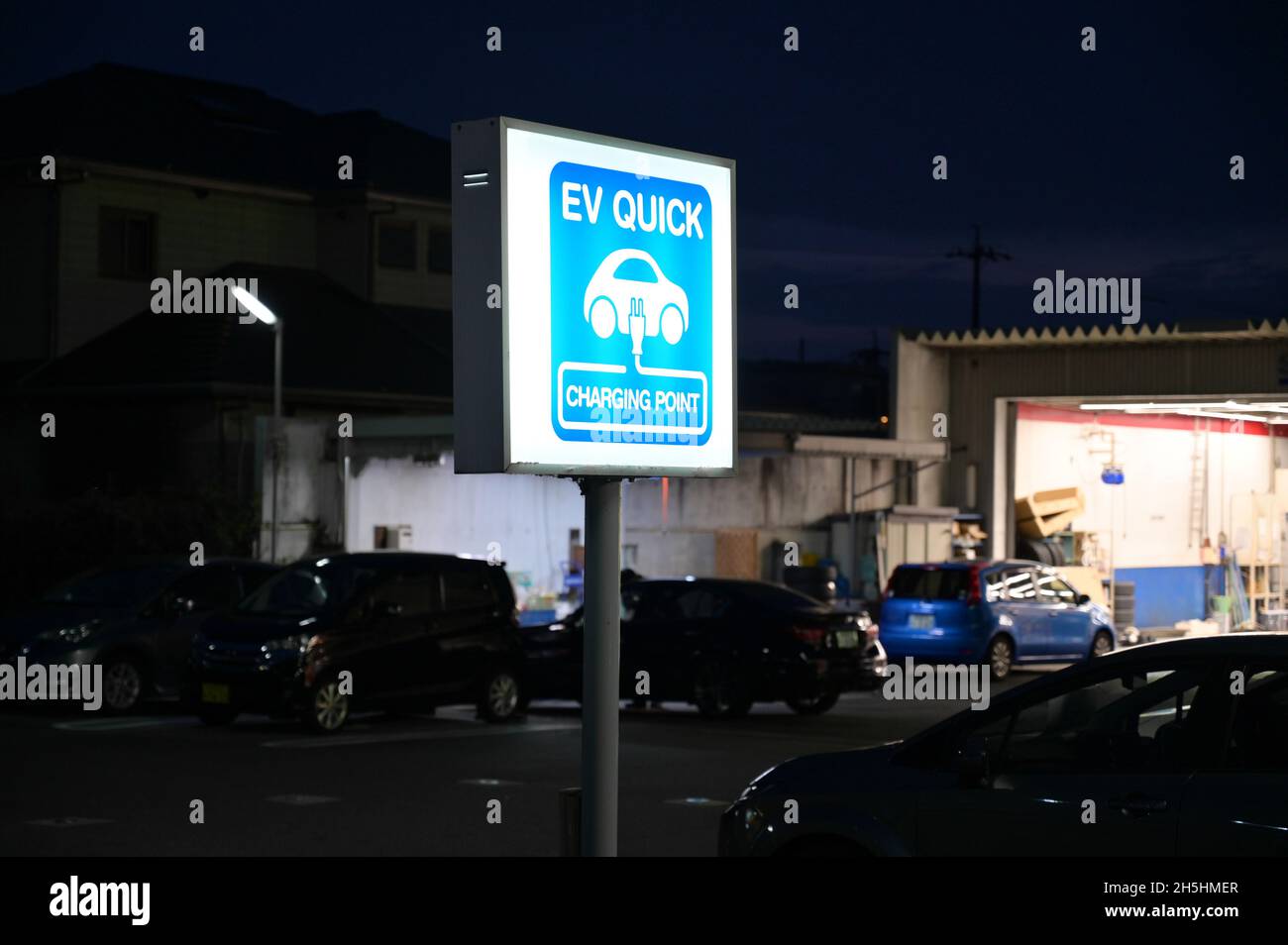EV Quick charging point for electric vehicles. Blue light up sign. Repair shop in the background. Stock Photo