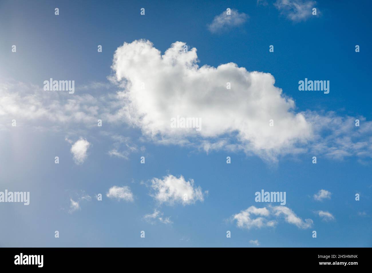 A single fleecy cloud, along with a few feathery clouds, adorns the blue sky in strong winds Stock Photo