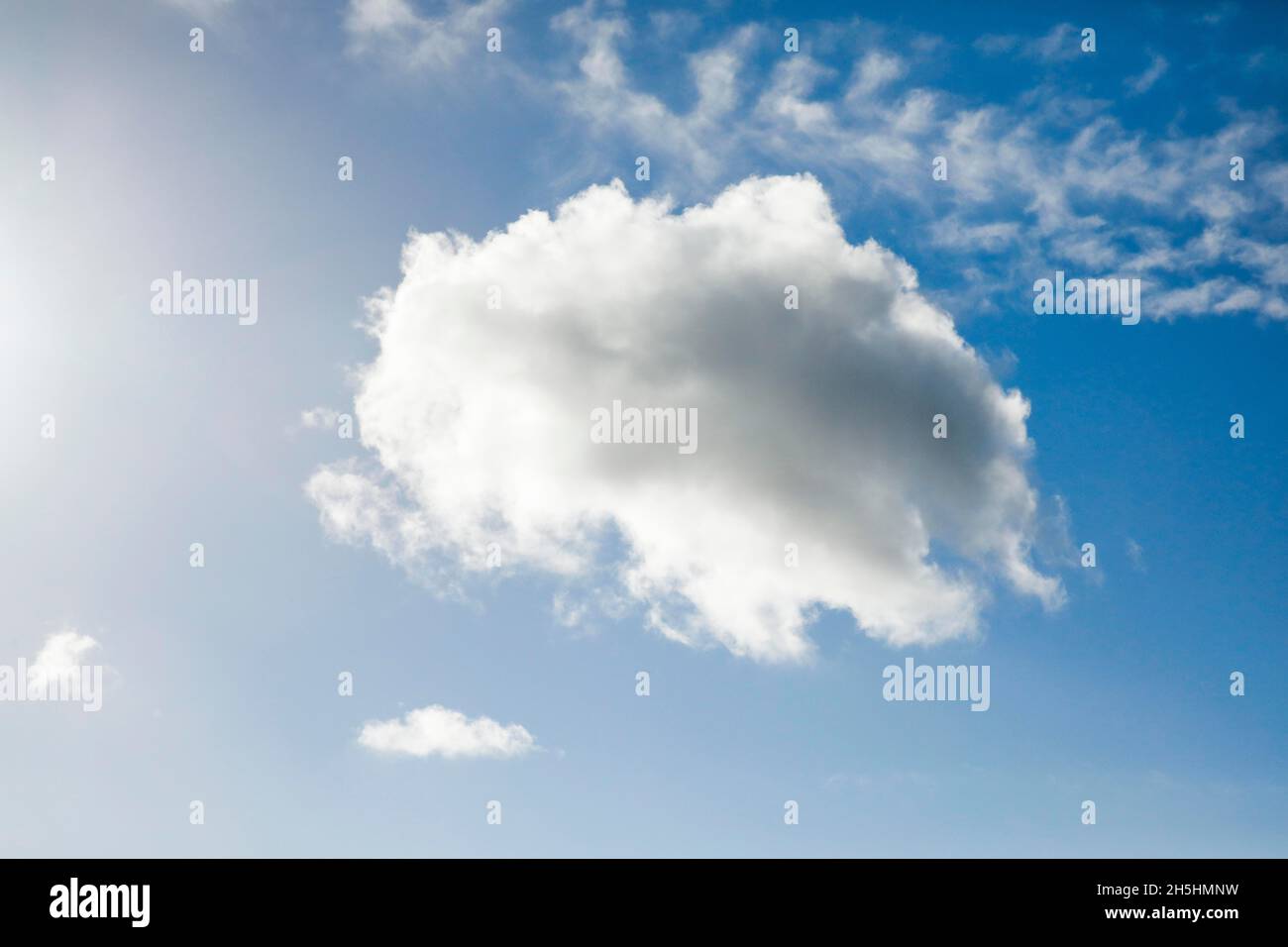 A single fleecy cloud, along with a few feathery clouds, adorns the blue sky in strong winds Stock Photo