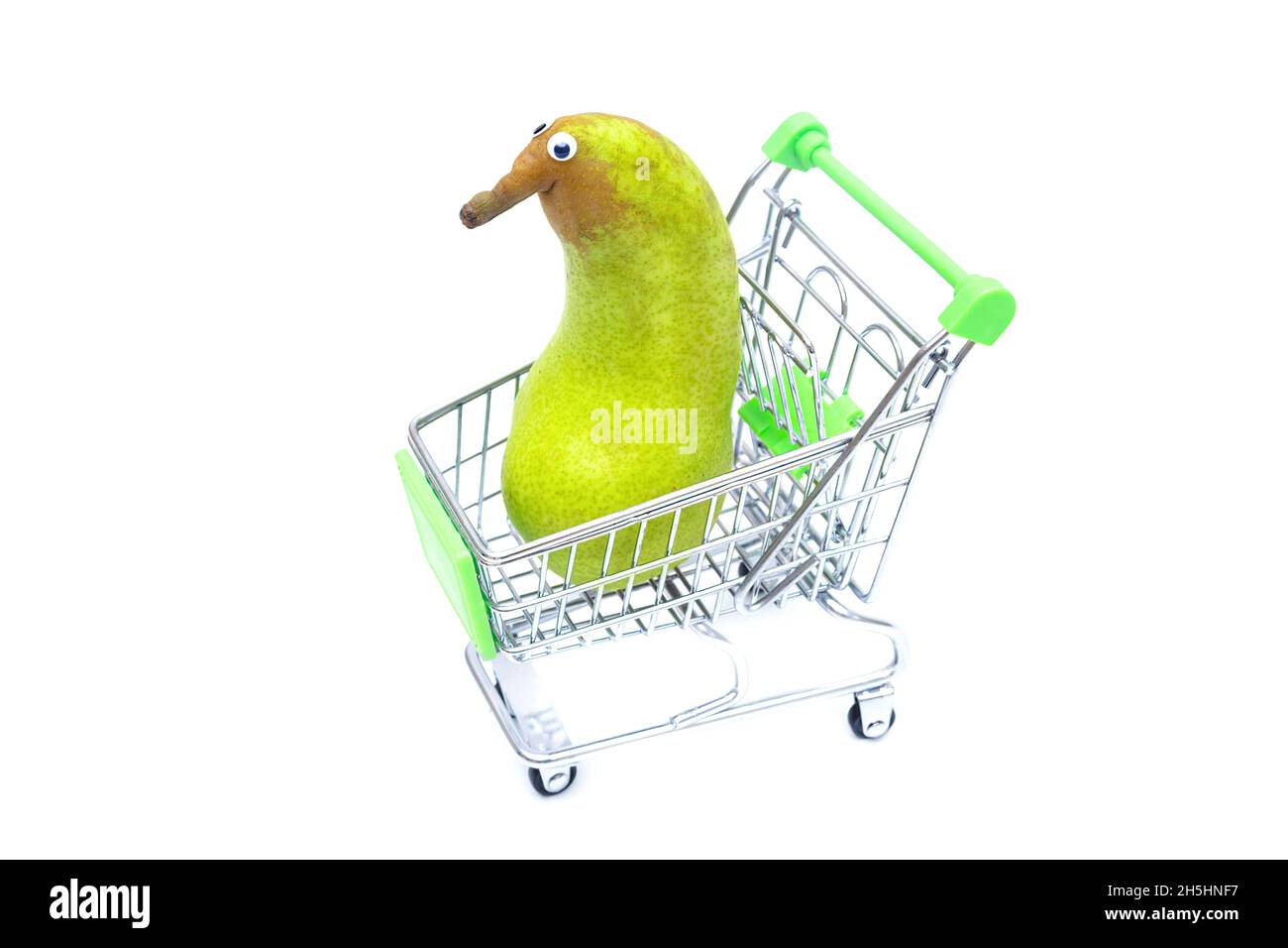 Anthropomorphic pear with googly eyes in a small shopping cart isolated on white. Stock Photo