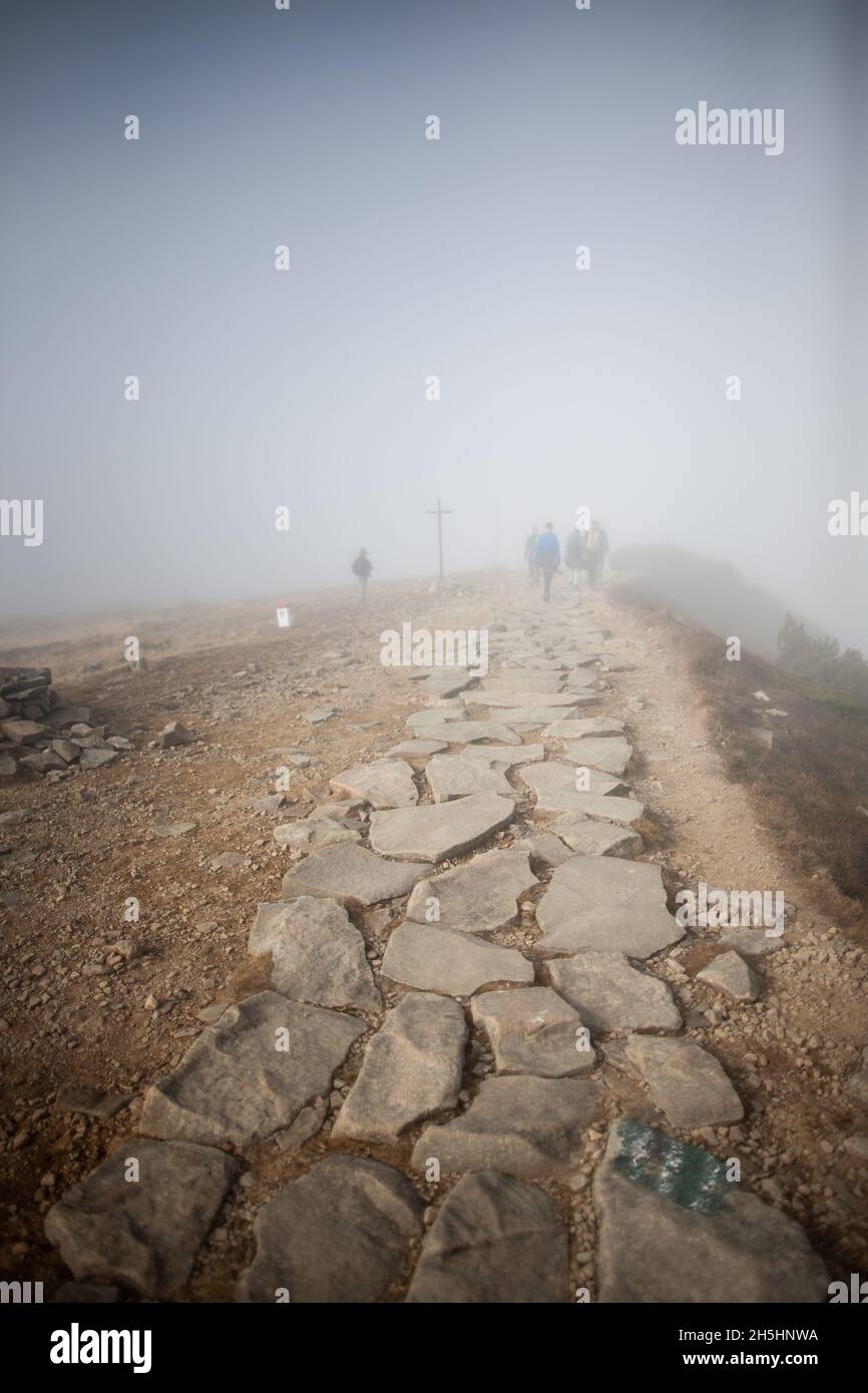 Tourists walk in thick fog in the mountains | Group of people in the fog by the cross on the mountain trail, Stunning view Amazing weather Stock Photo
