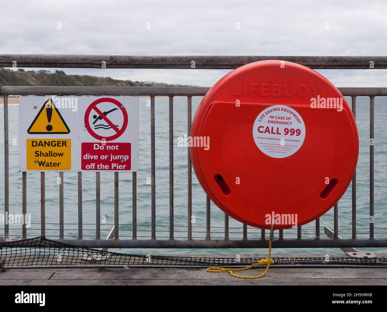 Lifebuoy life saving equipment and warning notices fixed to metal railings on Boscombe pier. Dorset, England, UK Stock Photo