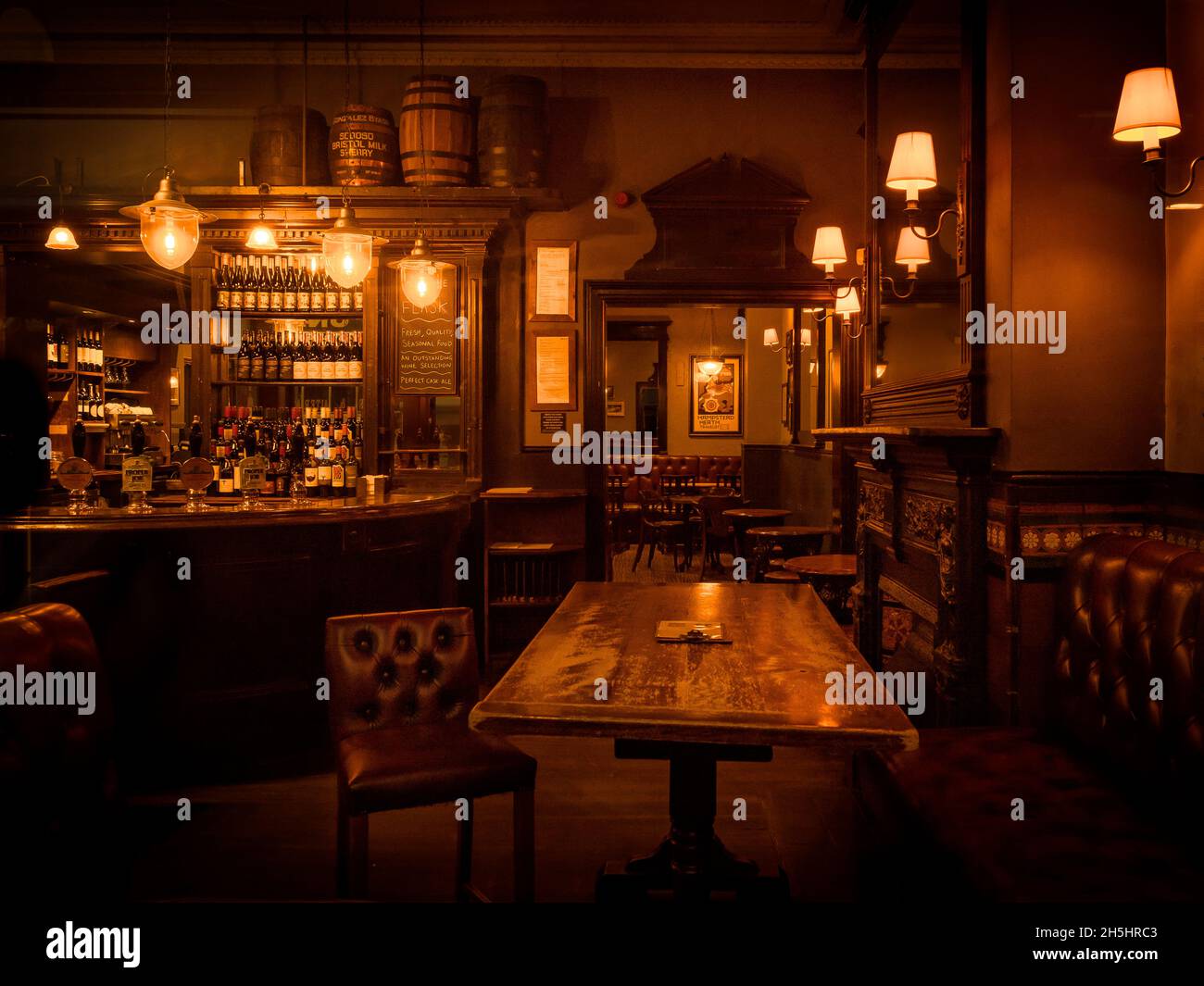 An atmospheric and moody old, empty bar with wooden panelling and. tables and leather chairs in The Flask pub on Flask Walk, Hampstead, London. Stock Photo