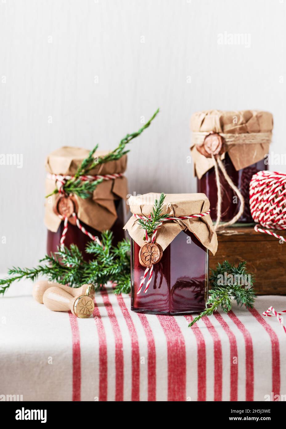 Handmade gift for Christmas. Homemade fruit jam in the jars decorated with grunge paper, wax seal and green twig of coniferous tree. Stock Photo