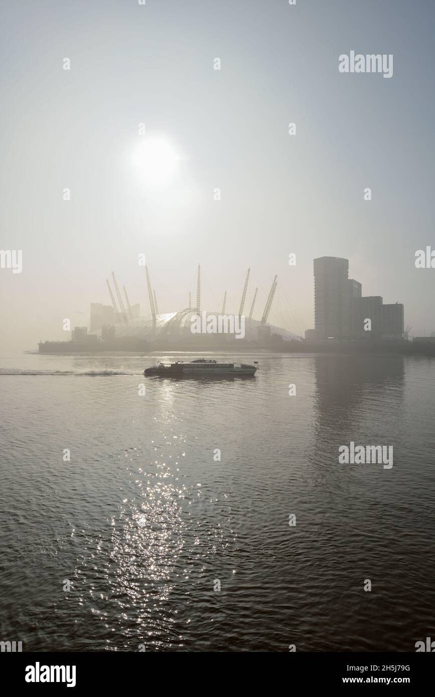 Misty early morning Thames river, Uber Boat Thames Clippers river ferry and the O2 Arena entertainment venue, Greenwich Peninsula, East London, United Stock Photo