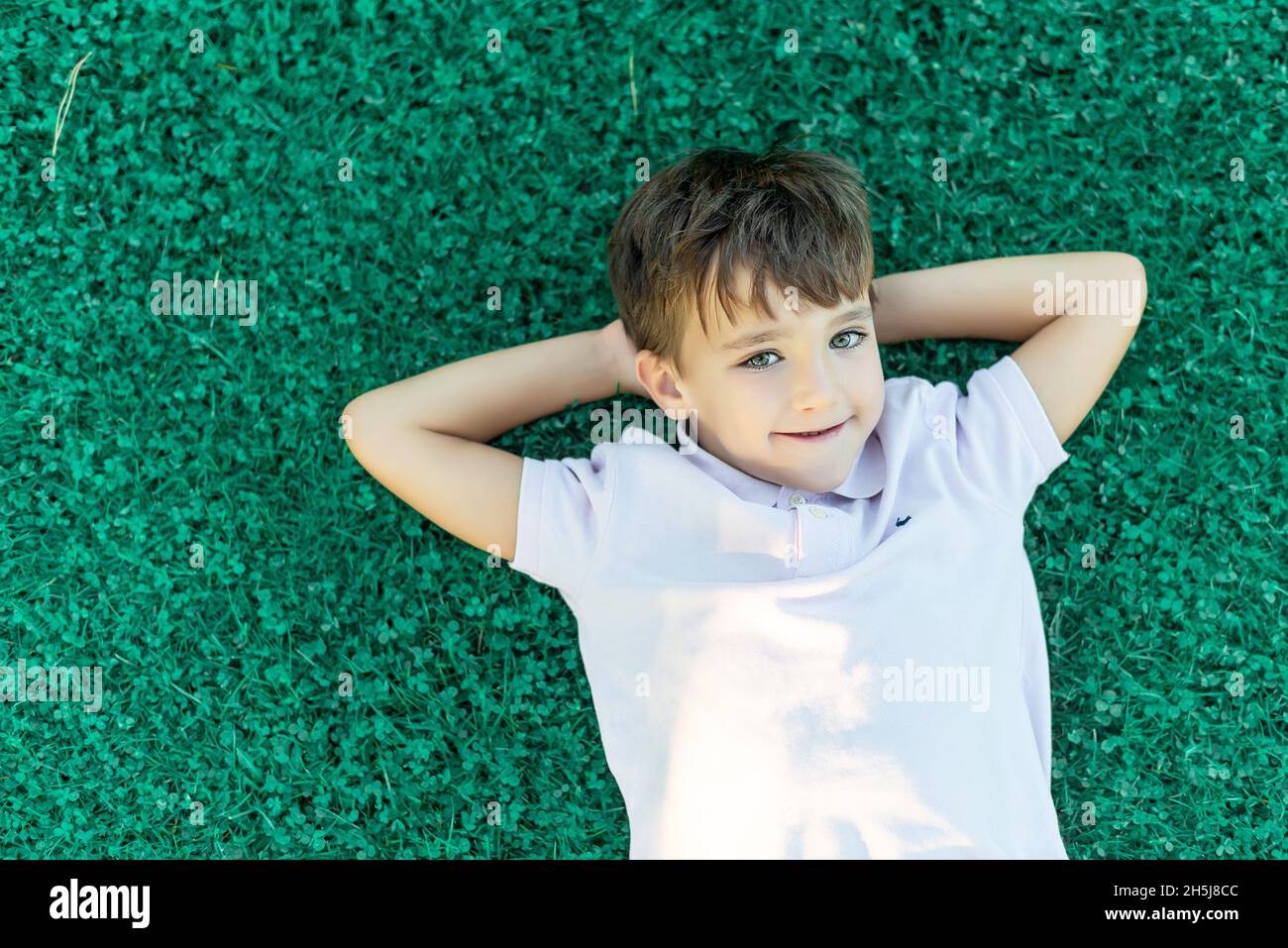 Smiling green-eyed boy lying on the grass with his hands on the back of his head Stock Photo