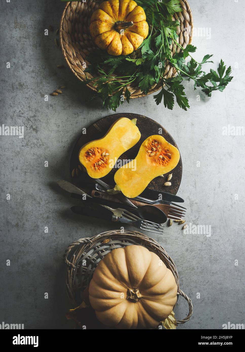 Halve of butternut squash on pale grey kitchen table with millet in bowl and kitchen utensils. Preparing healthy vegan millet porridge at home with se Stock Photo