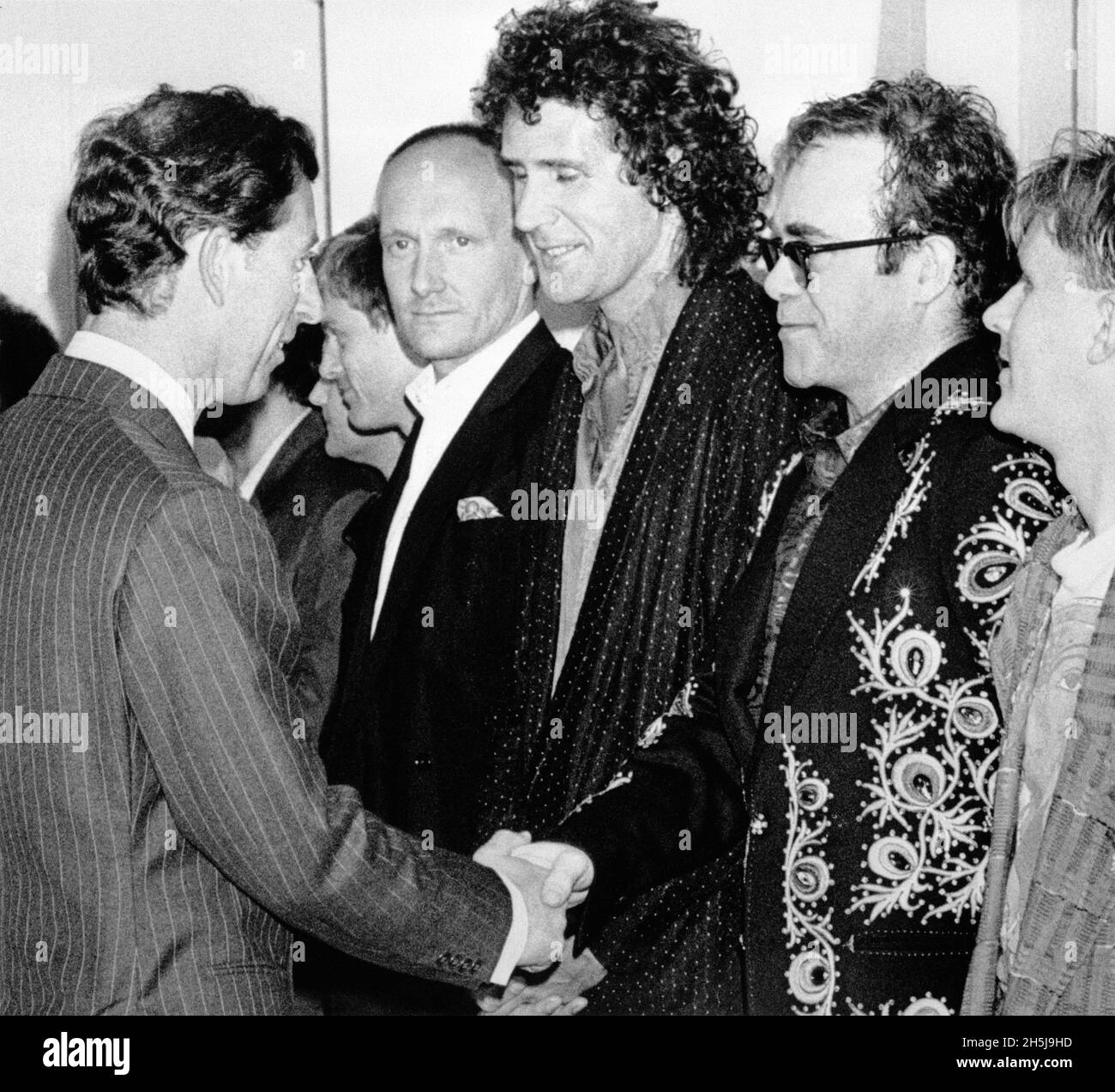 File photo dated 20/6/1986 of the Prince of Wales shaking hands with Elton John, flanked by his drummer Ray Cooper (left) and Dire Strait's bassist John Illsley (centre) before a rock extravaganza at Wembley to celebrate 10 years of the Prince's Trust. The two have met again at a Windsor Castle Investiture where the Prince made the musician a member of the Order of the Companions of Honour. Issue date: Wednesday November 10, 2021. Stock Photo