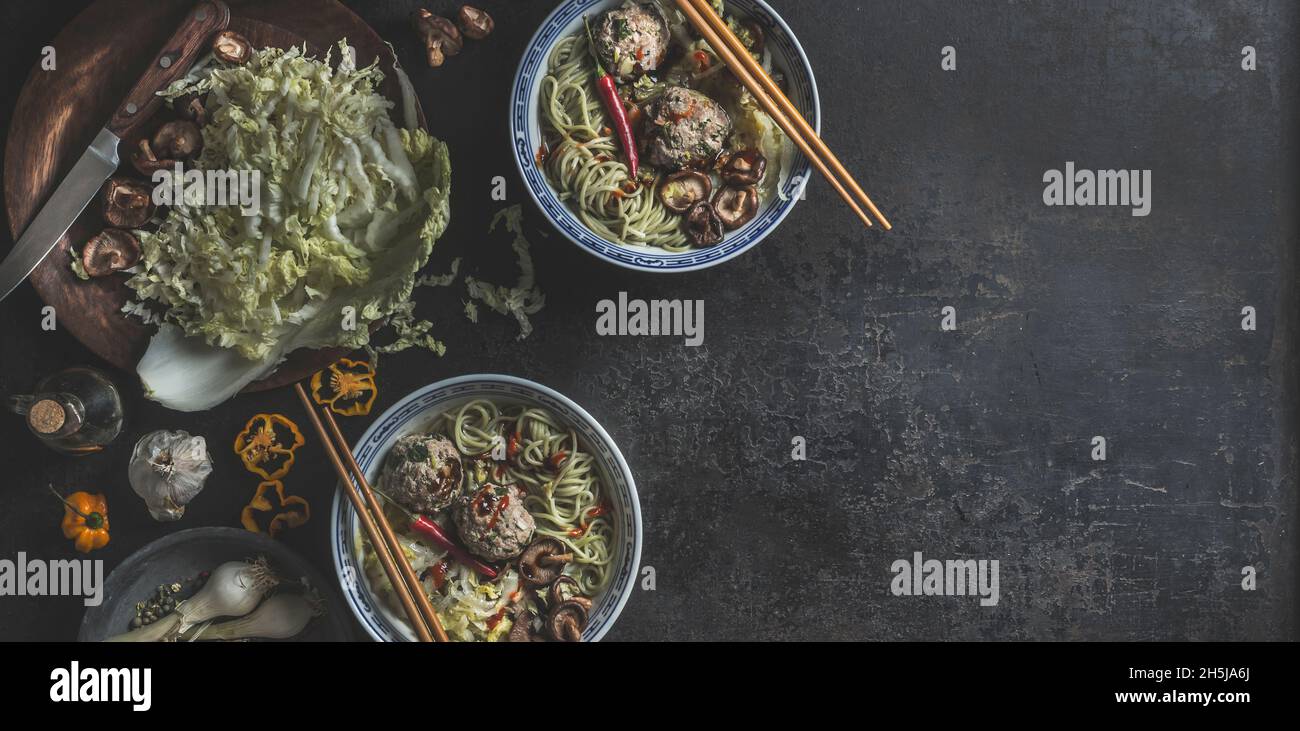 Bowls with Asian soup with cabbage, mushrooms, shiitake, garlic, chili and dumpling in traditional crockery with chopsticks on dark concrete table. Fo Stock Photo