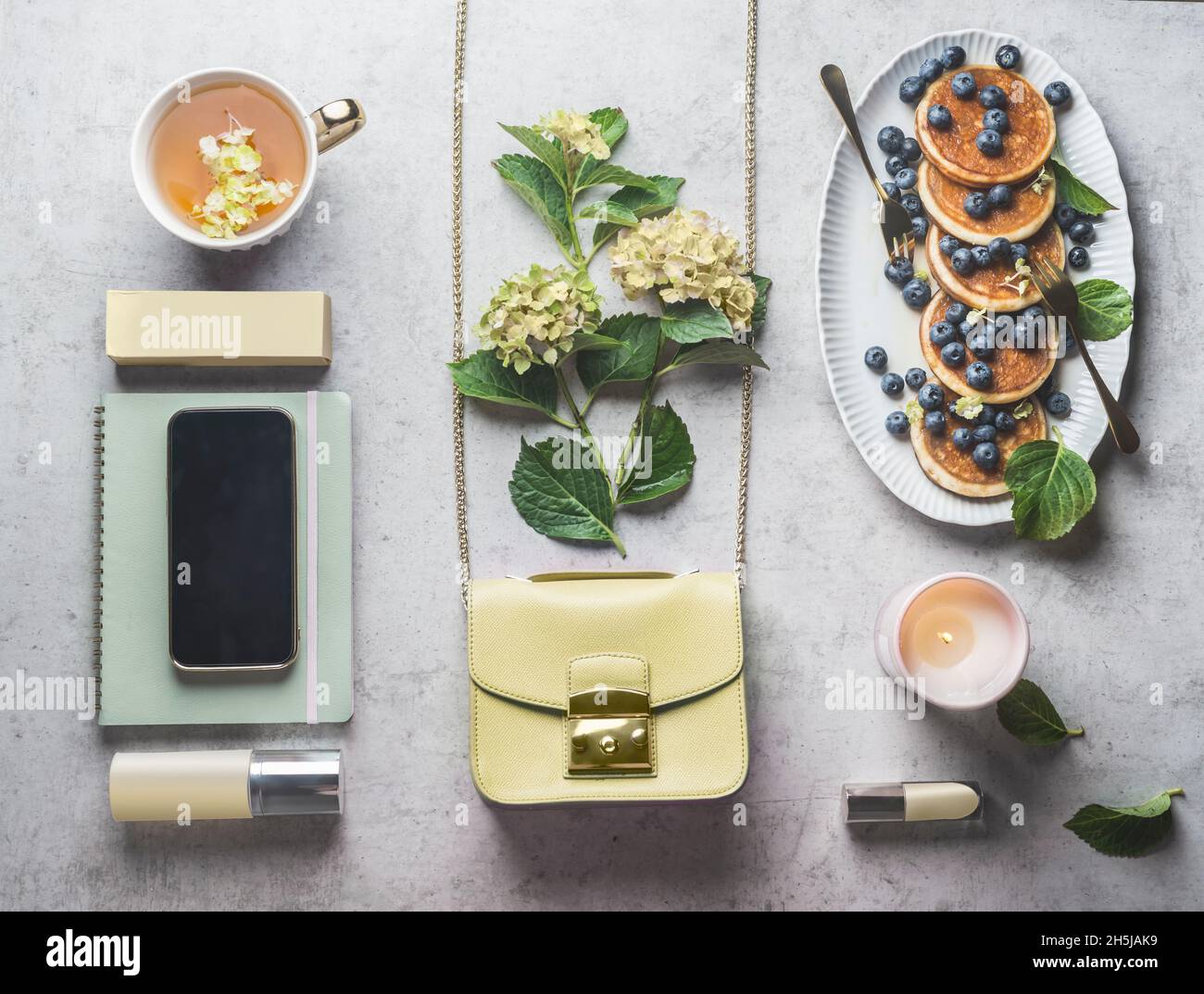 Stylish feminine background with smartphone, handbag, lipstick, tea, pancakes and notebook on pale grey table. Freelancer concept with breakfast and c Stock Photo