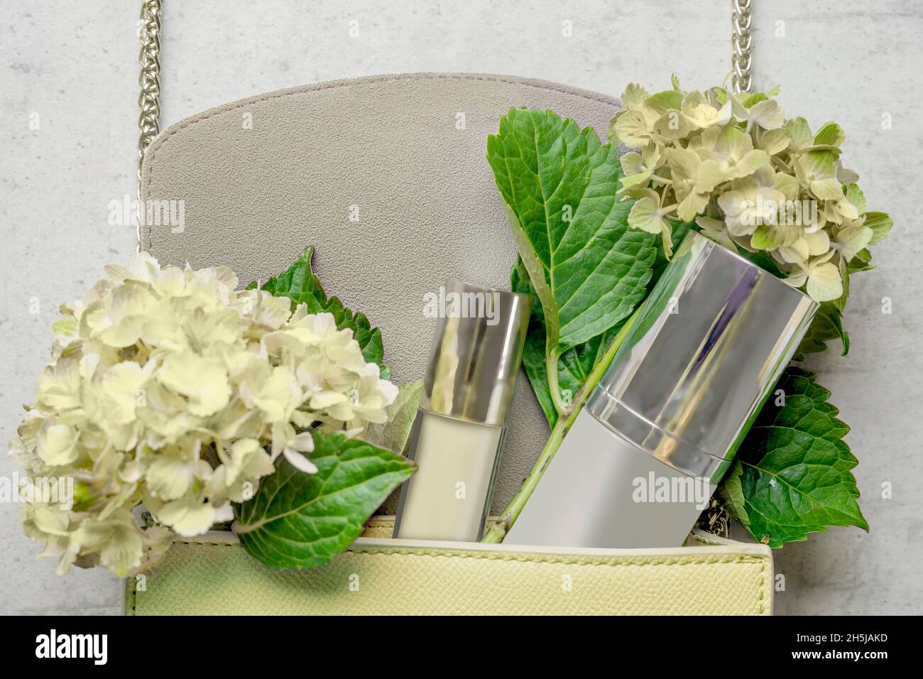 Pale yellow handbag with cosmetic bottle, lipgloss and hydrangea flowers on white wooden background. Feminine lifestyle concept. Top view. Stock Photo