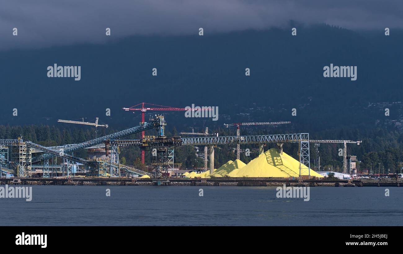 View of huge stock pile of bright yellow colored Sulphur (S) at bulk cargo terminal in North Vancouver, British Columbia, Canada with conveyor belts. Stock Photo