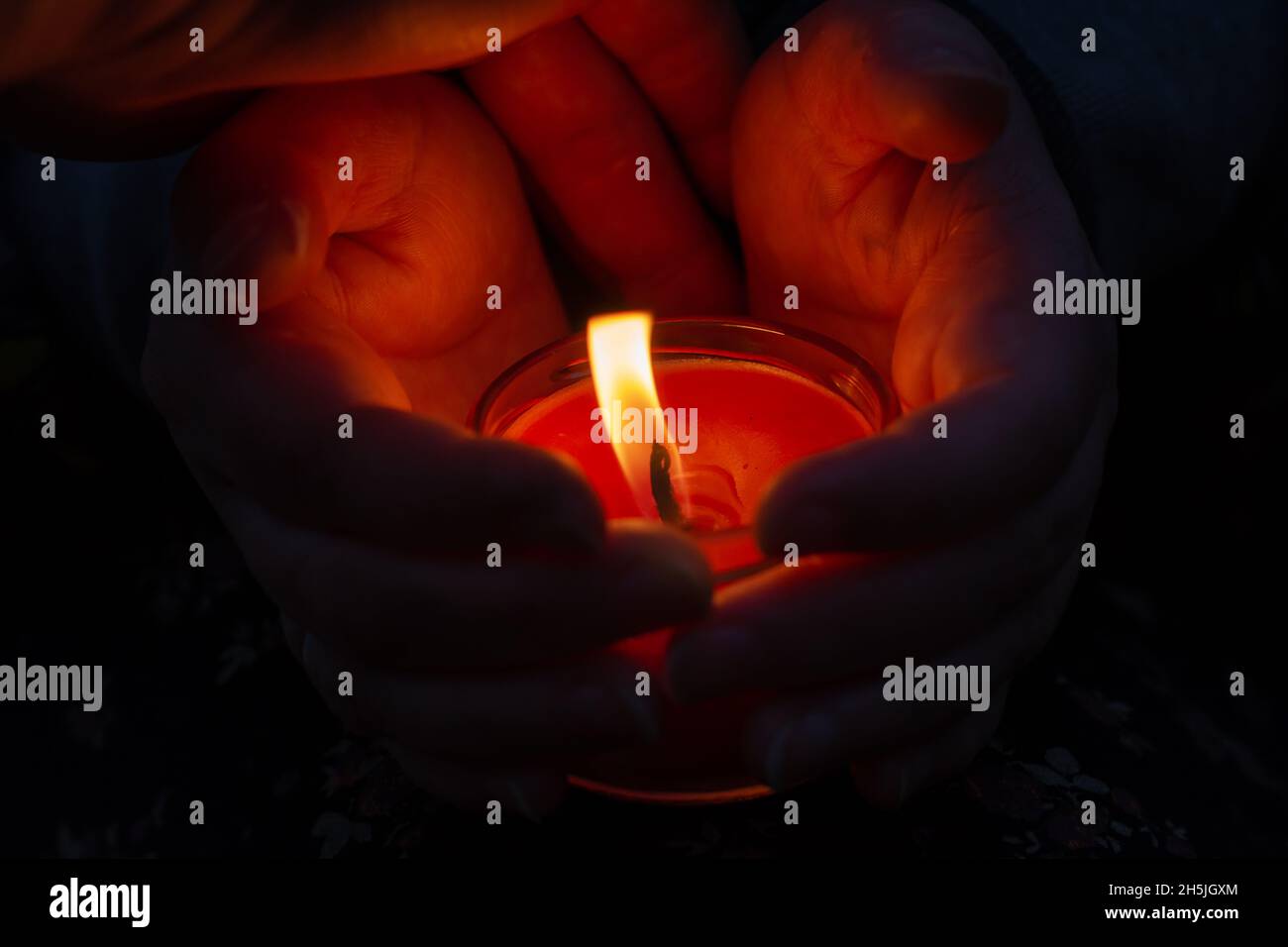 A red burning candle between a woman's palms. The woman shelters the