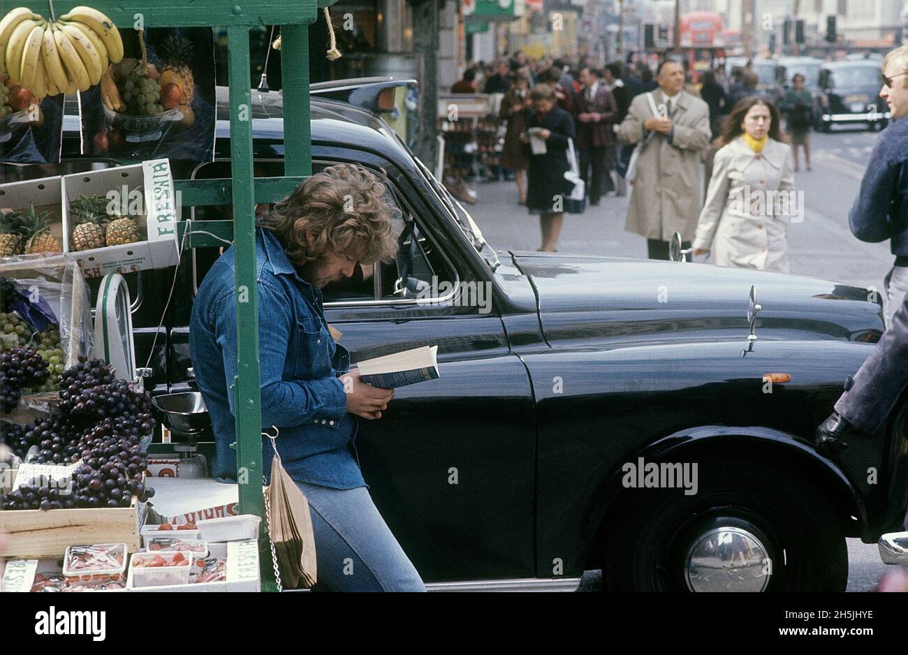 London 1982. A street view of a London street with a stand filled with fruit for sale and a man reading a book while waiting for customers. Credit Roland Palm. Stock Photo