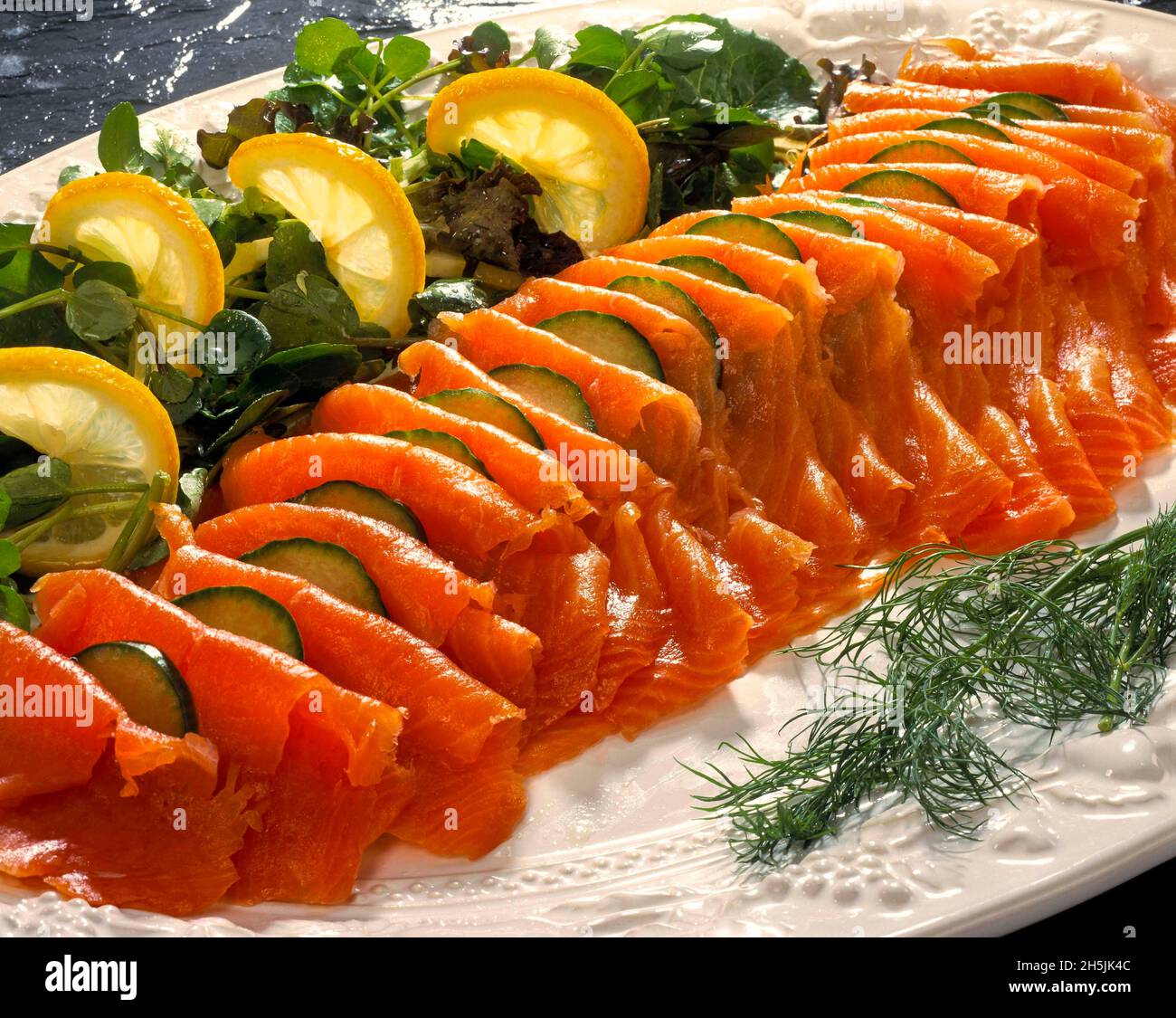 White Platter plate dish seafood smoked salmon slices fillet with lemon wedges fresh dill cucumber salad watercress Stock Photo