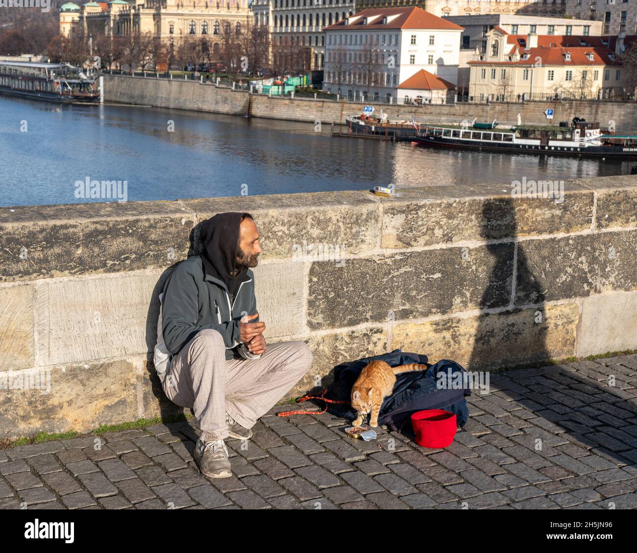 Prague, Czech Republic -January 14, 2020: Homeless man with a cat sitting on the Charles bridge begging for help and money. Problems of big modern cit Stock Photo