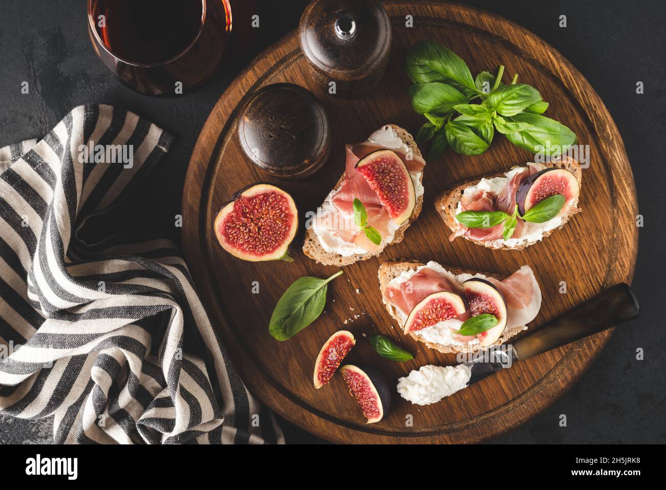 Italian appetizer bruschetta with ham prosciutto, cheese and figs on a wooden serving board, glass of red wine. Top view Stock Photo