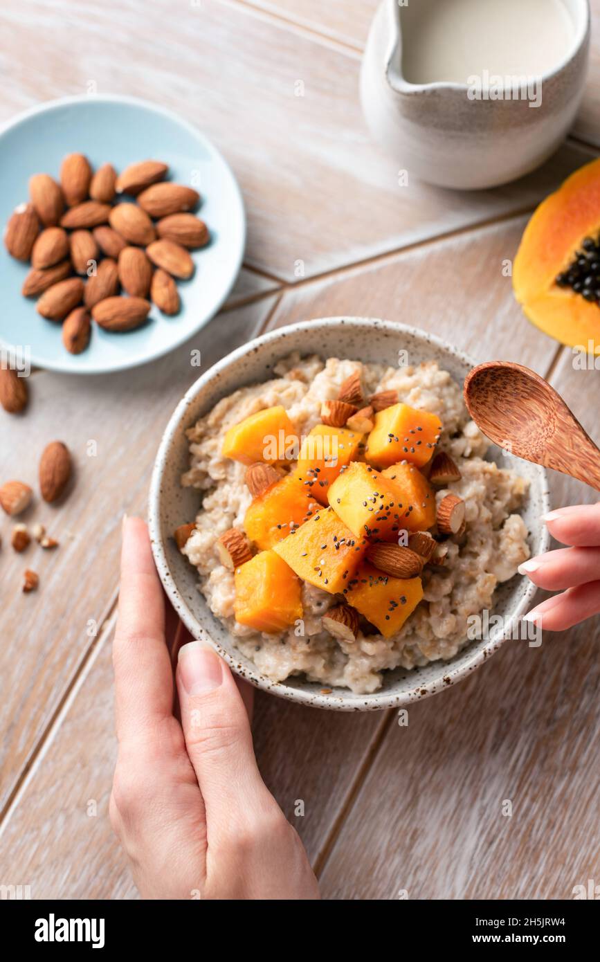 Oatmeal with chopped papaya, almonds and chia seeds in female hands. Healthy vegan breakfast bowl top view Stock Photo