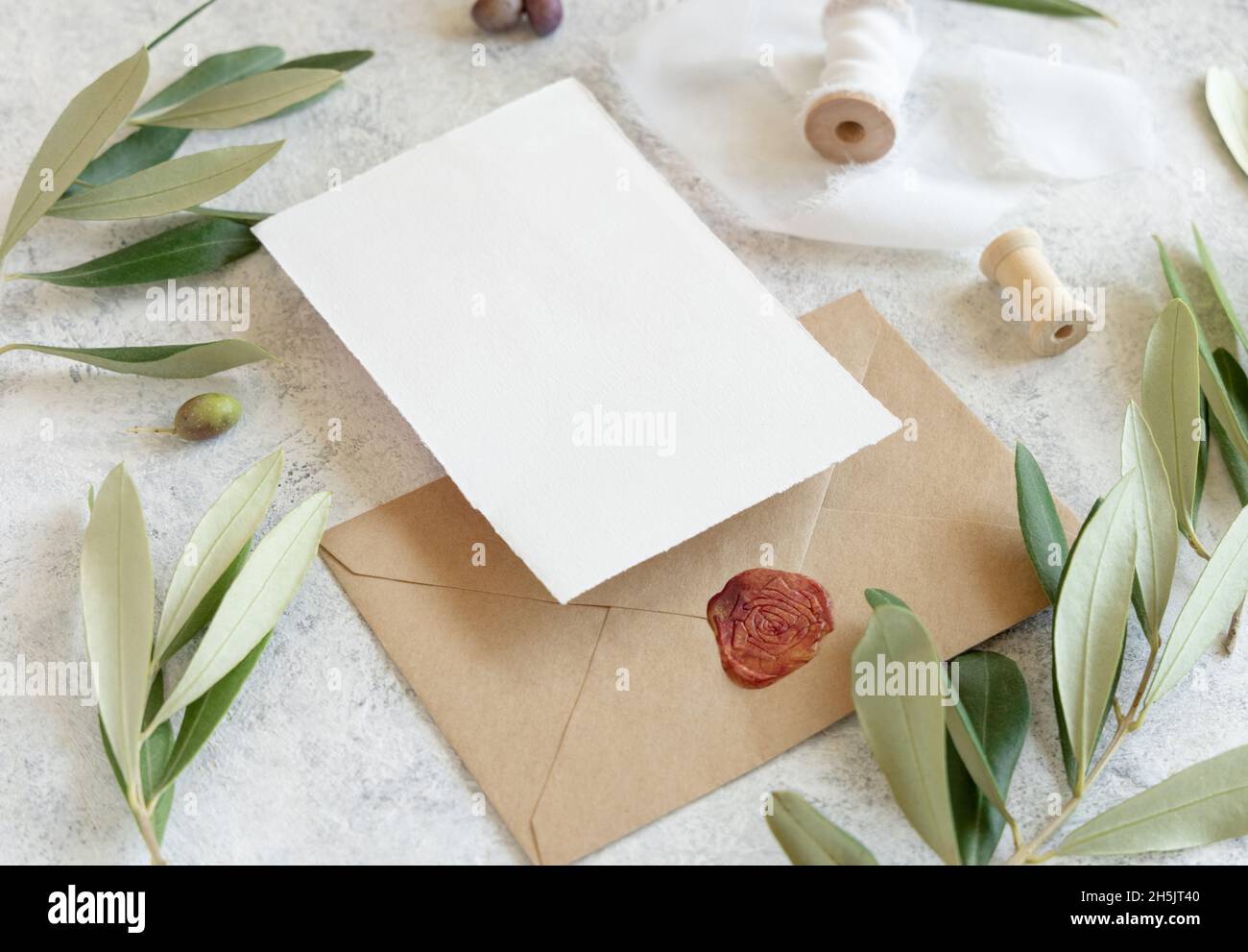 Wedding invitation cards and envelopes on a white marble table with olive branches close up. Elegant modern template with horizontal blank paper cards Stock Photo