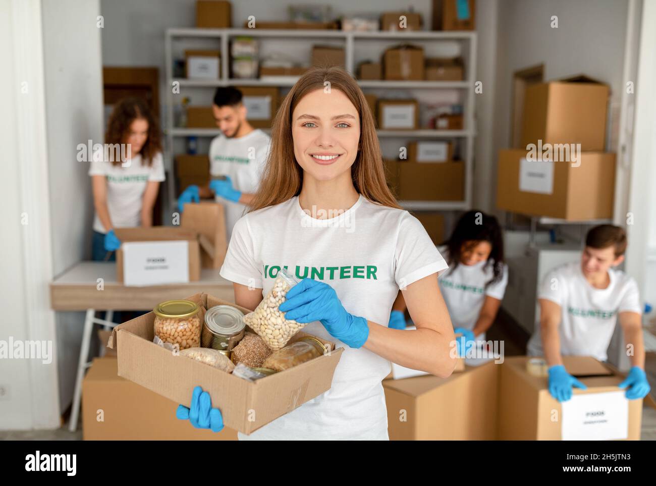 Happy female volunteer working at charity center, holding food donation