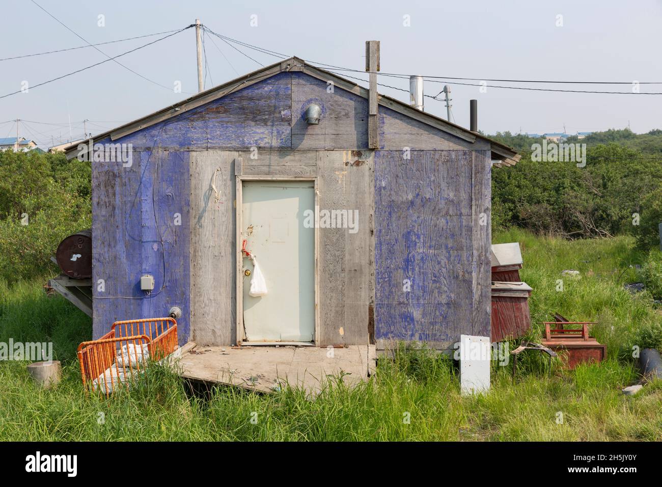 A weathered plywoodsided house is painted purple, a crib sites outside the door, Mountain