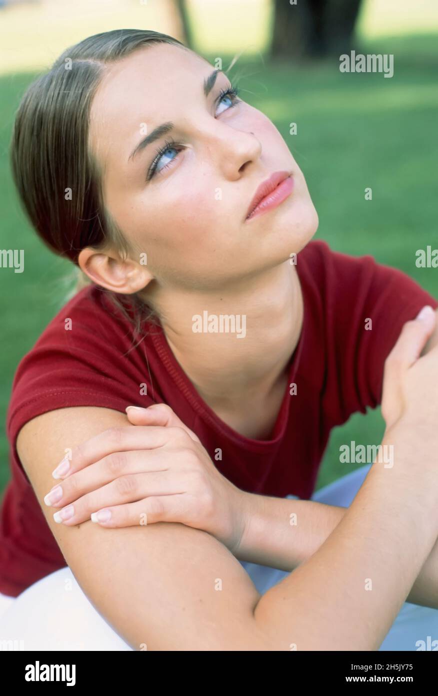 Teenage girl sitting outside looking up with a pensive expression; Germany Stock Photo