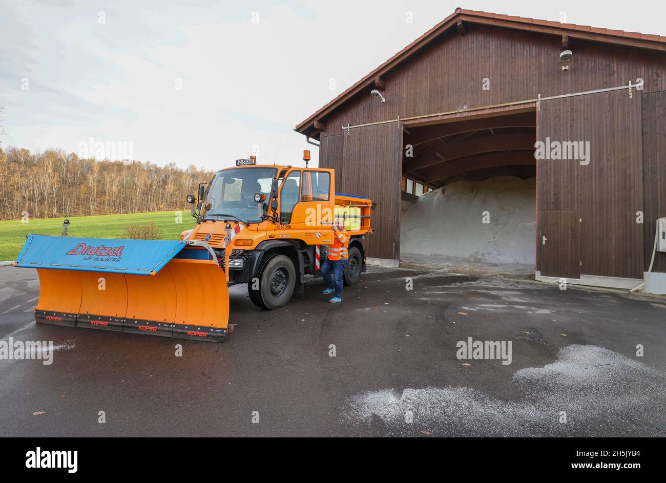 10 November 2021, Saxony, Zwickau: Road maintenance manager Sandro Wichmann mounts a clearing vehicle in front of the salt storage hall. The hall stores 1,000 tons of road salt; the district has stored 3,250 tons for the winter and has concluded contracts for the supply. The road maintenance department, with 25 employees, looks after 789 kilometres of country, state and district roads. Already last night, the first vehicles went out to spread salt in the highlands against the slippery roads caused by the night frost. Photo: Jan Woitas/dpa-Zentralbild/dpa Stock Photo