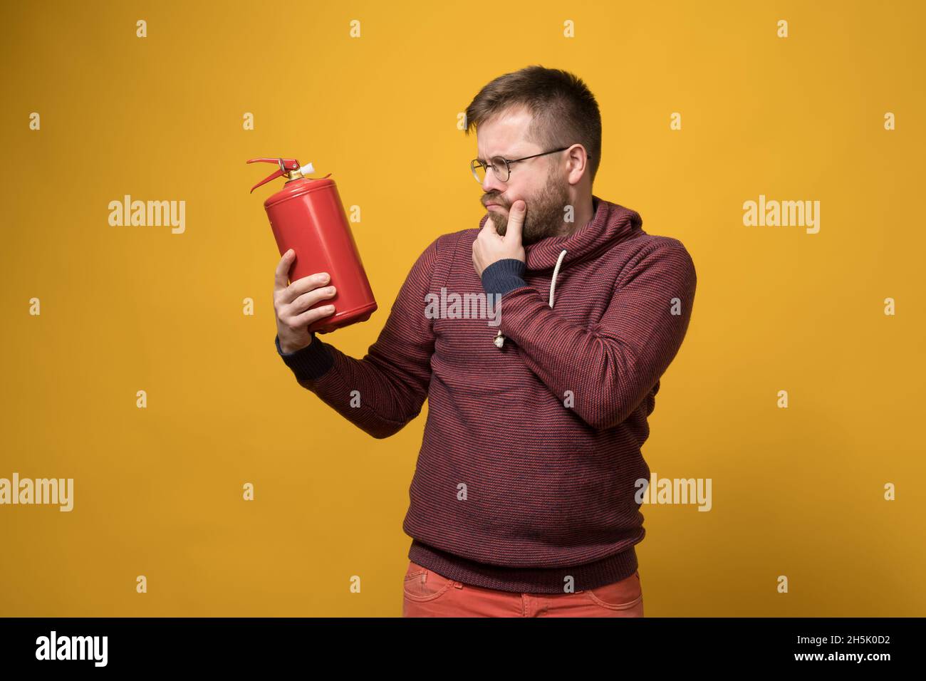 Puzzled man with glasses holds a fire extinguisher in hand and looks at