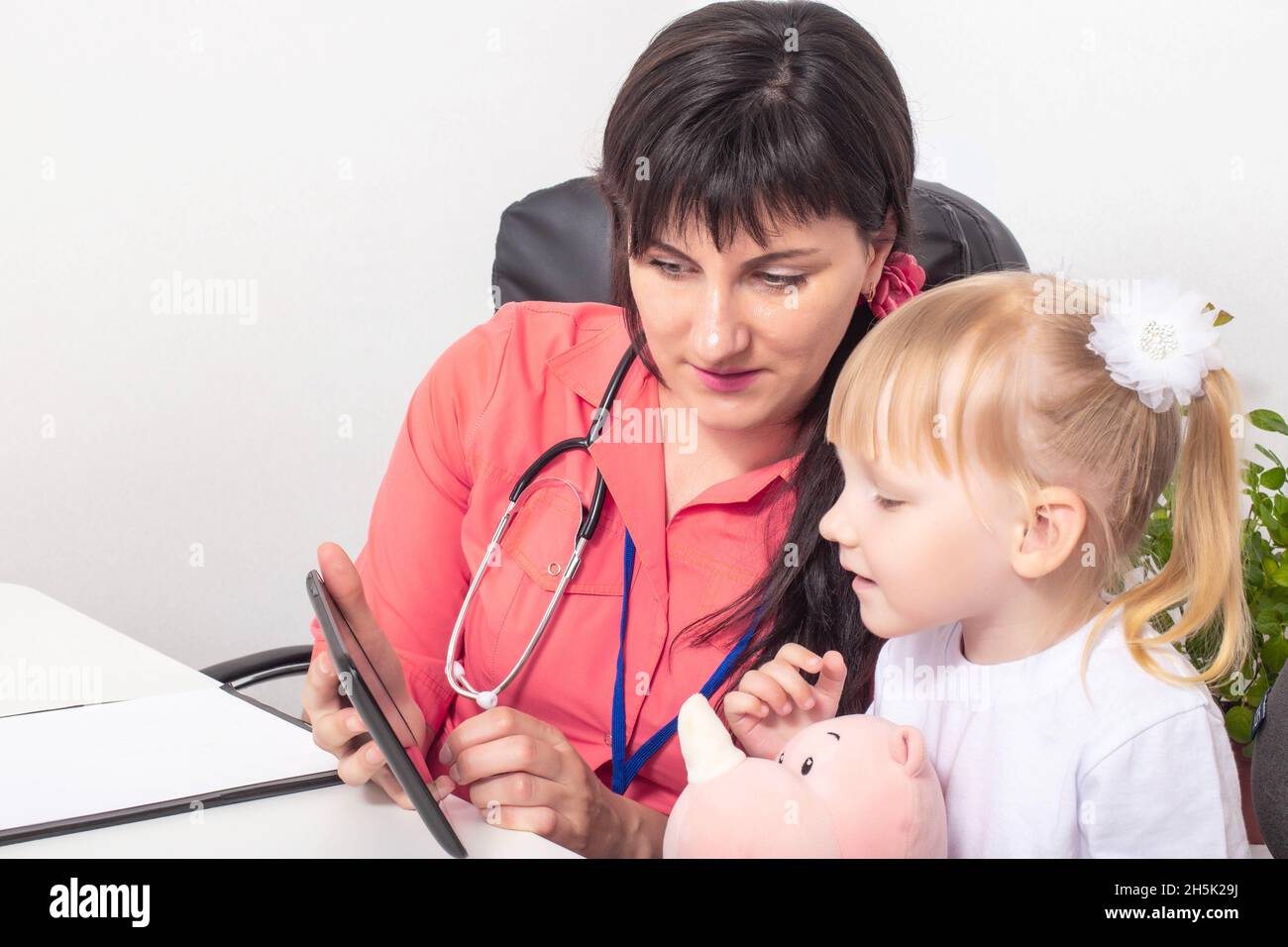 Doctor pediatrician shows cartoons on the tablet of a little girl 3-4 years old. The concept of psychological contact with a child at a doctor Stock Photo
