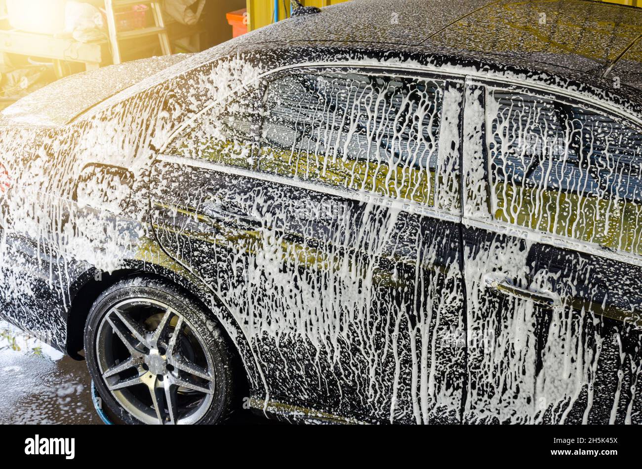 Black dirty car in white soap foam at car wash service station