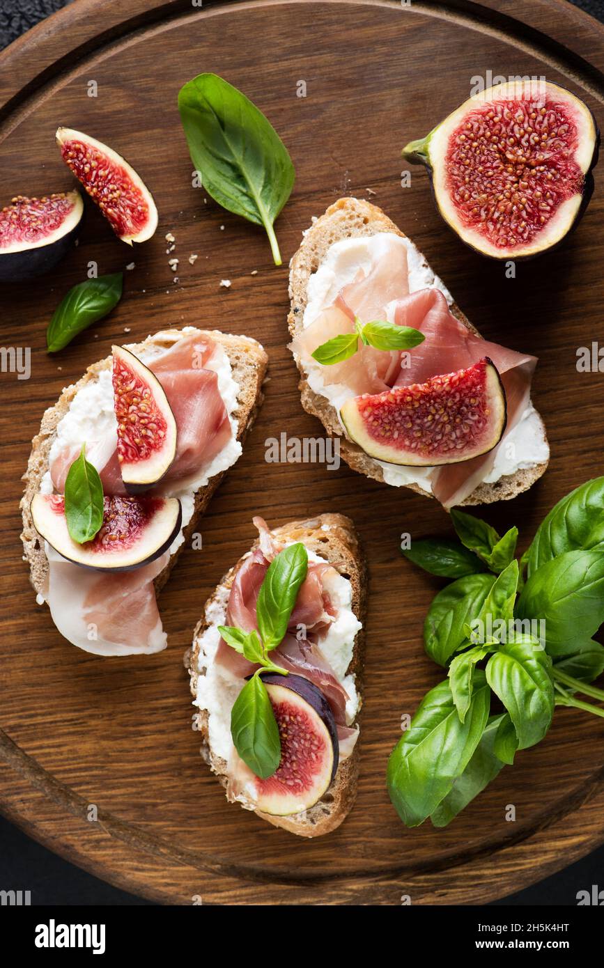 Bruschetta with ham, fig and ricotta cheese on a wooden serving board. Italian appetizer or snack Stock Photo