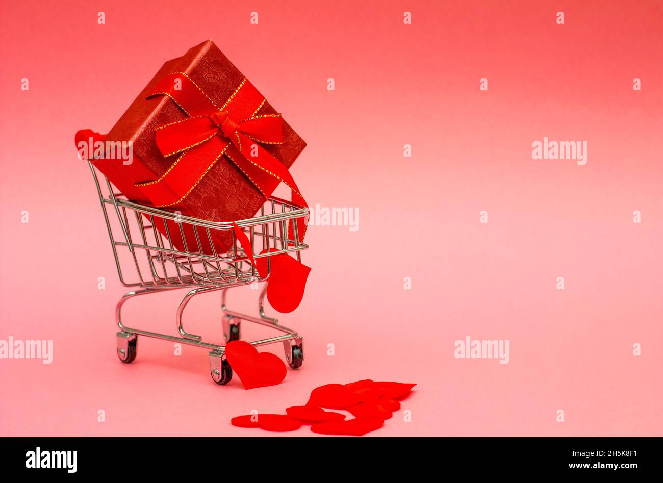 Gifts in a red box with a red ribbon, hearts and a bow. Creative concept with a shopping trolley with gifts, on a red background. place for your text. Stock Photo