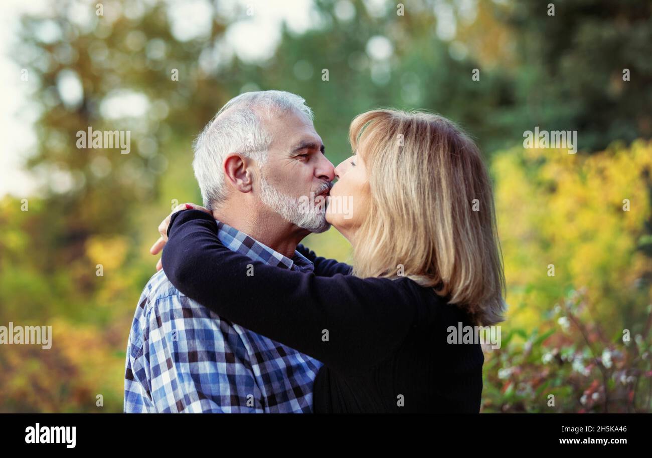 A mature couple enjoying time together and stopping to kiss while walking in a city park on a warm fall evening; St. Albert, Alberta, Canada Stock Photo