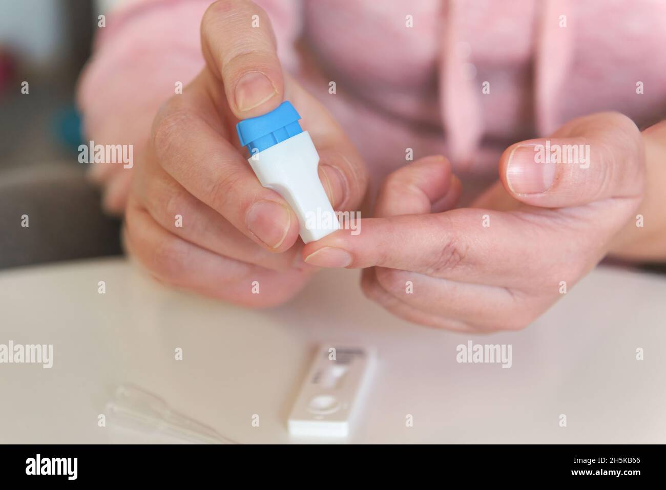 The woman uses a lancing device to take a blood sample from her finger and test for COVID19 or diabetes Stock Photo