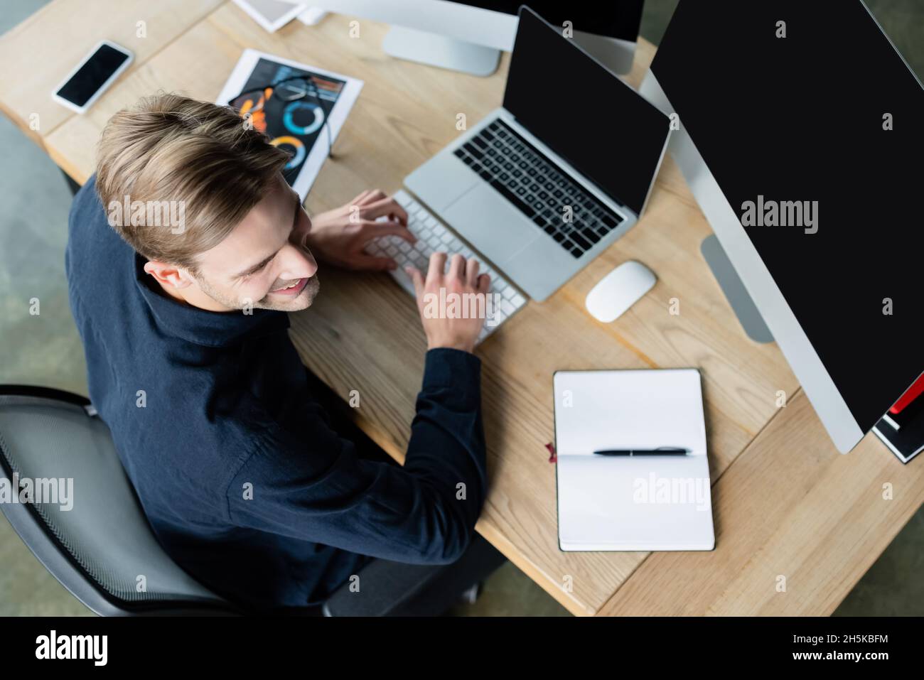 Overhead view of smiling developer using computers near smartphone and notebook on table Stock Photo
