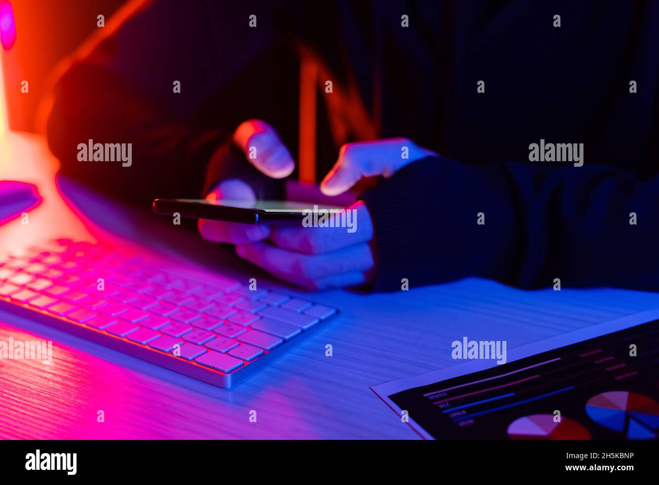 Cropped view of programmer using smartphone near computer keyboard and document on black background Stock Photo