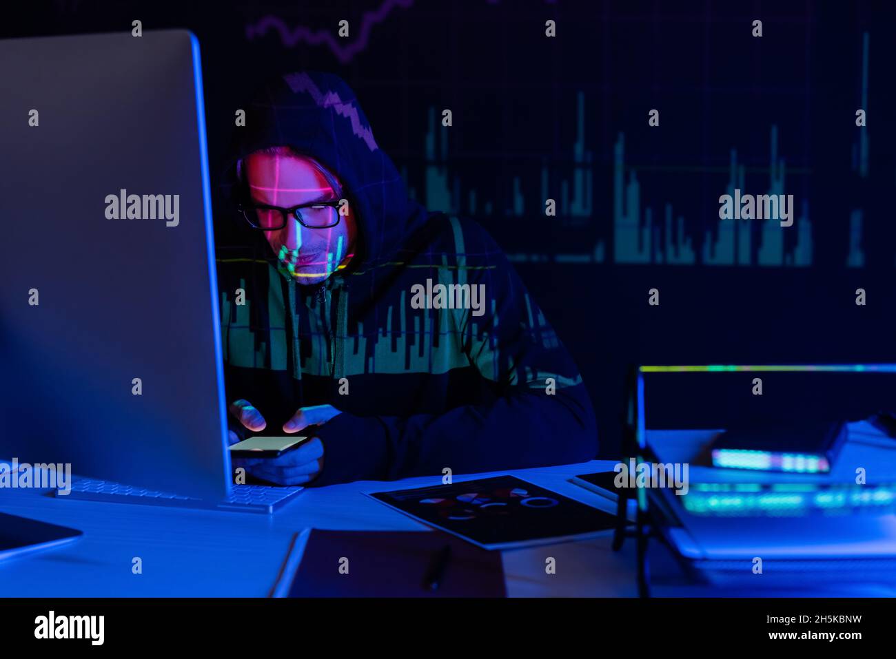 Hacker with charts reflection using smartphone near computer and documents on black background Stock Photo