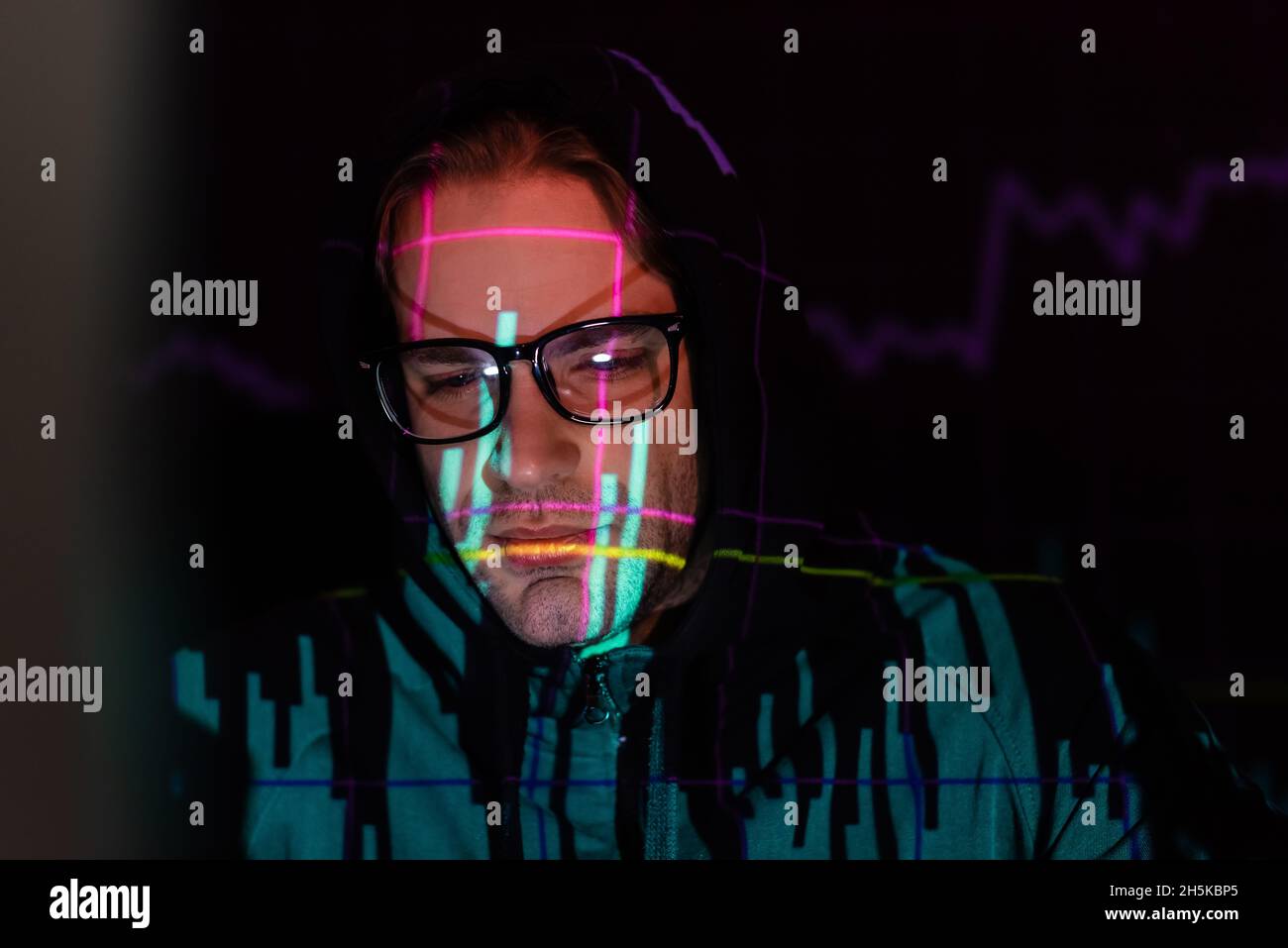 Displeased hacker with charts reflection looking down on black background Stock Photo