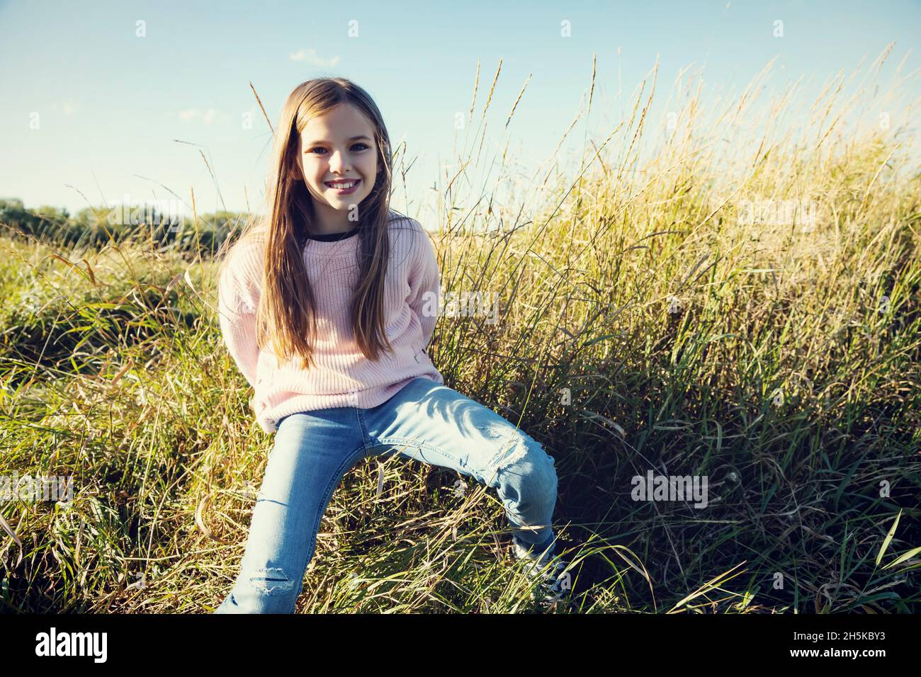 Portrait of a young girl sitting in the tall grasses on a field in the countryside; Alcomdale, Alberta, Canada Stock Photo