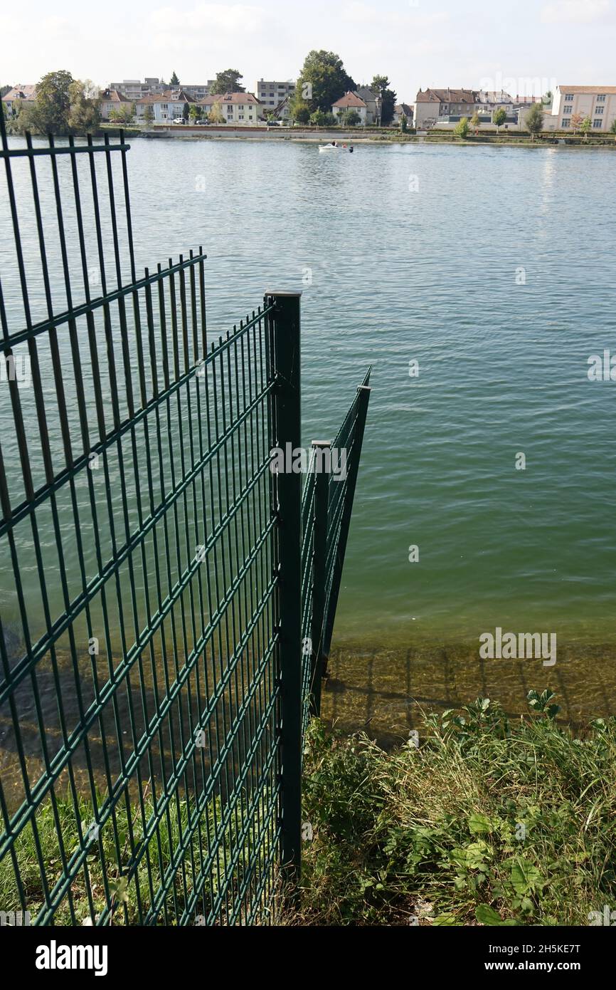 Mesh wire fence marking the Swiss German border at Kleinhüningen Rhine port with the Swiss German French border triangle in the middle of the river Stock Photo