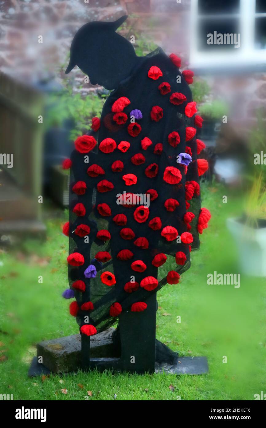 A metal figure of a first world war soldier covered with poppies in remembrance of service men lost in war. Stock Photo