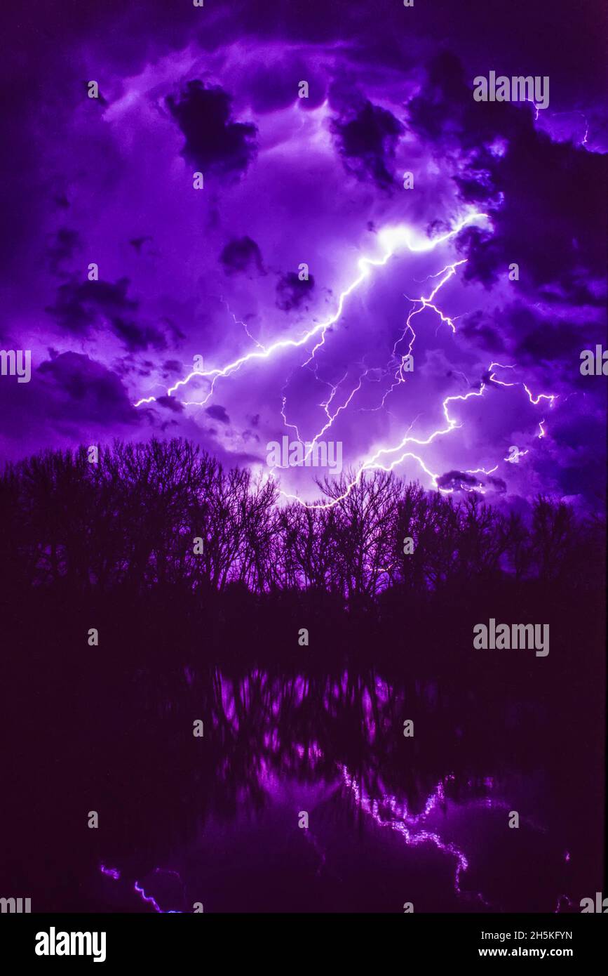 Lightning bolts illuminating a moody night sky reflecting in the water; Nebraska, United States of America Stock Photo