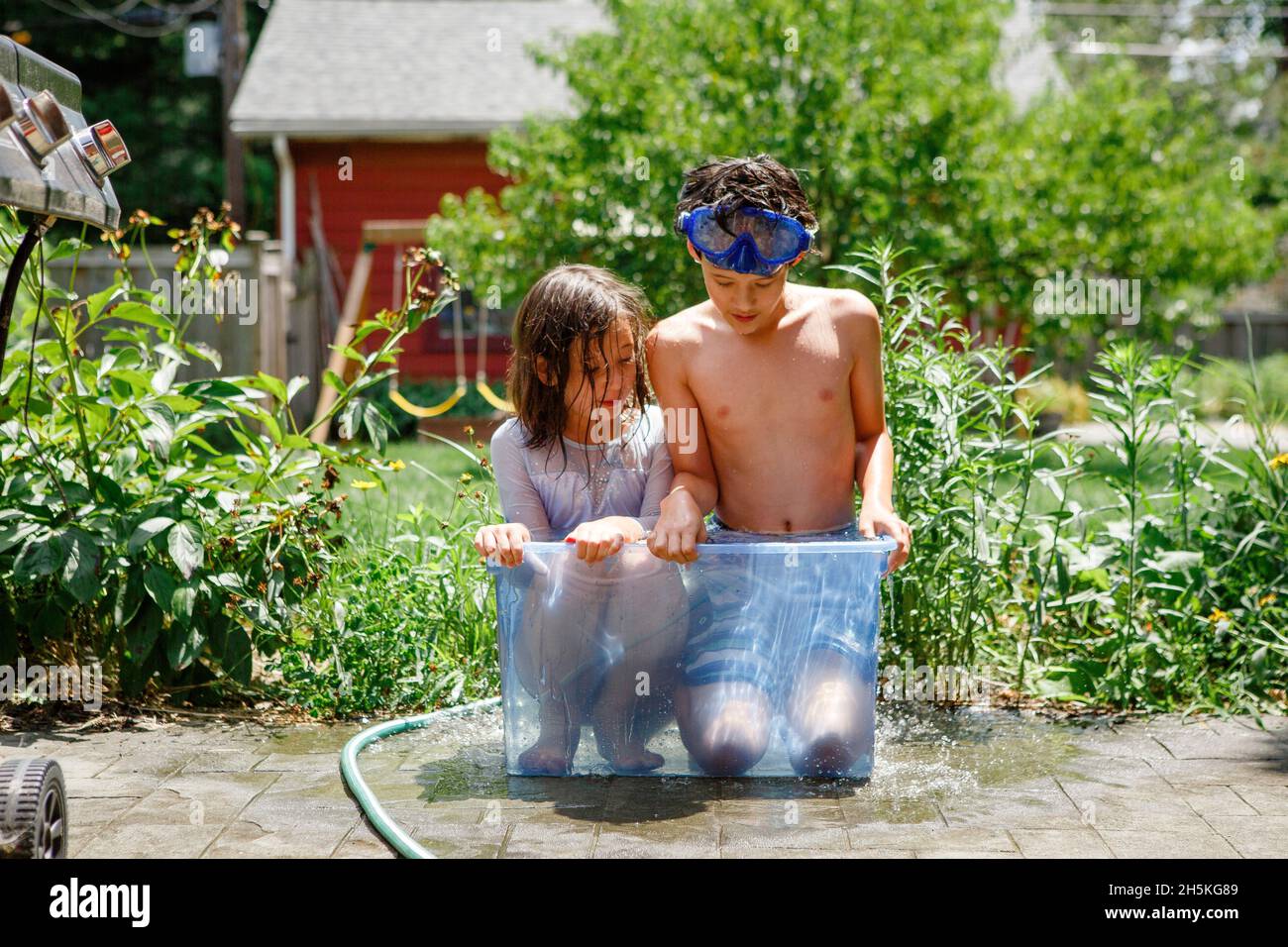 A boy and girl in bathing suits squeeze together in small tub of water