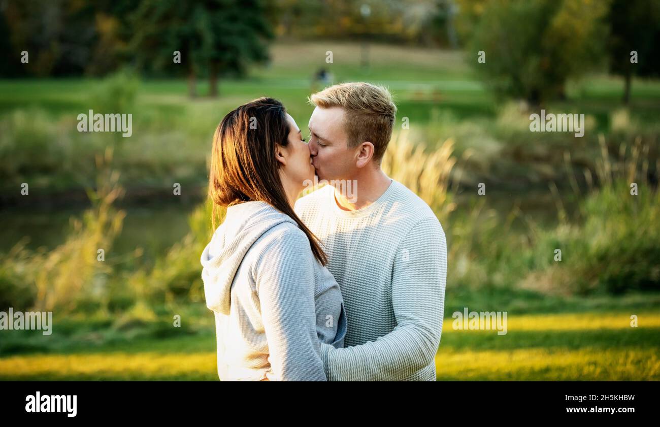 A mid adult couple sharing a kiss in a park at sunset; St. Albert, Alberta, Canada Stock Photo