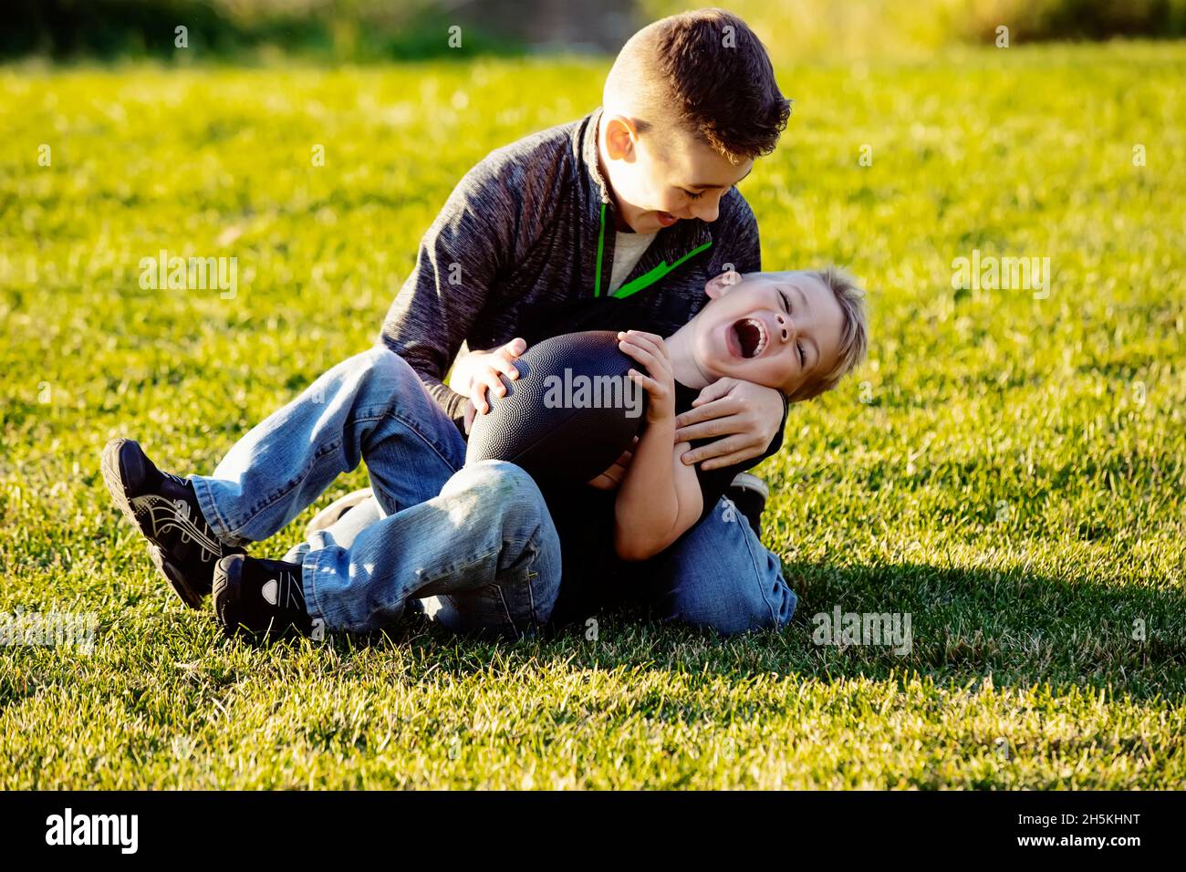 Two brothers roughhousing on the grass with a football; St. Albert, Alberta, Canada Stock Photo